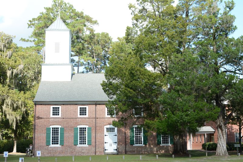 The red brick church and its white steeple among tall trees on a sunny day