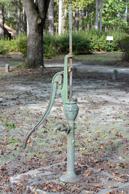 Old green cast-iron hand pump on sandy ground under trees