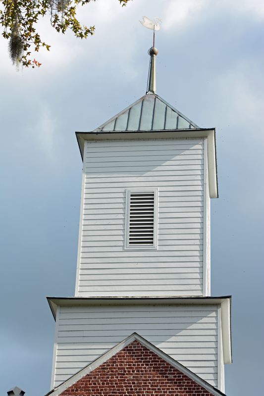 White wooden belfry with a louvered opening and a weathervane against the sky